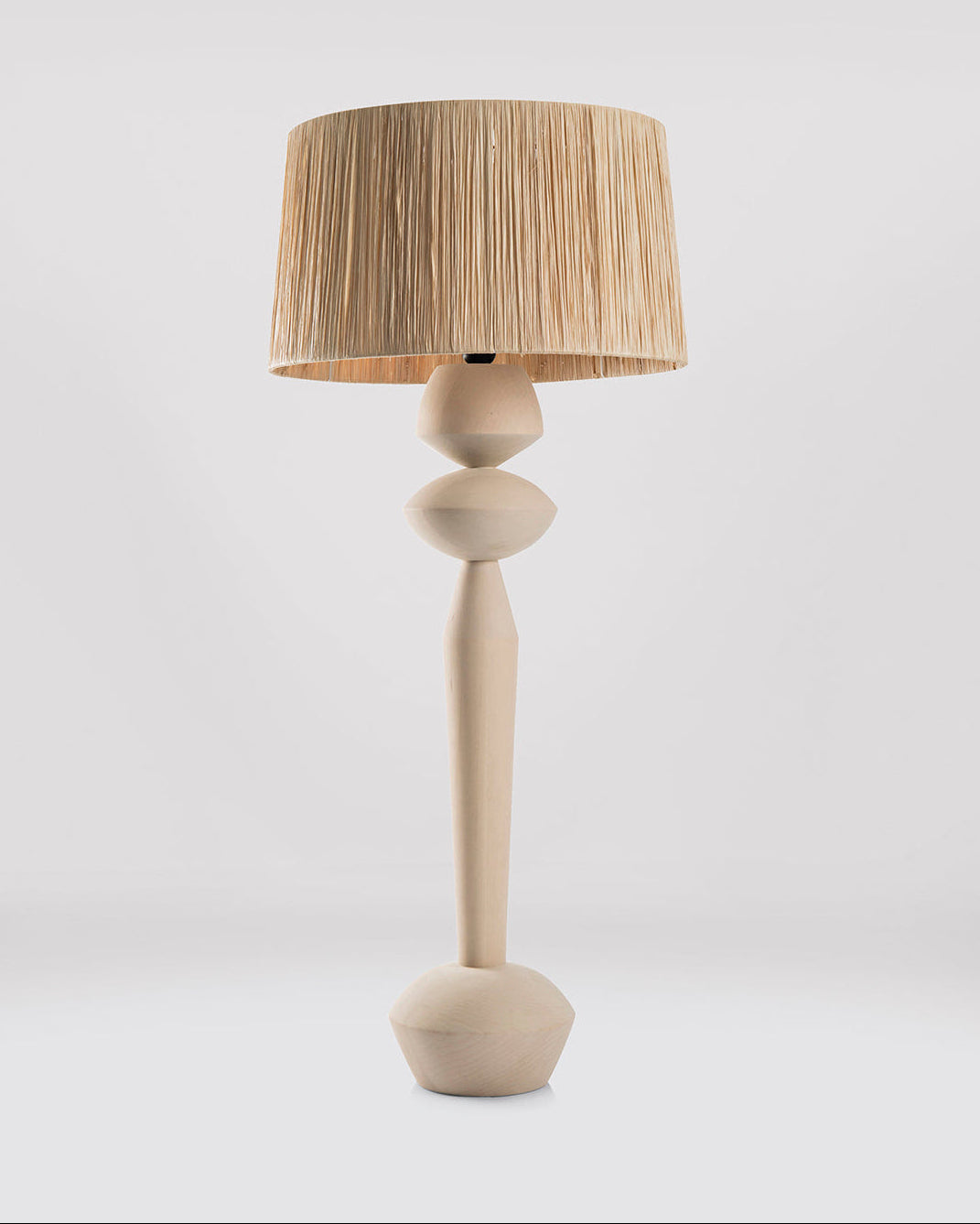 A modern table lamp with a sculptural, rounded wooden base in a light natural finish and a pleated drum shade in a warm beige tone, set against a seamless light gray studio background.